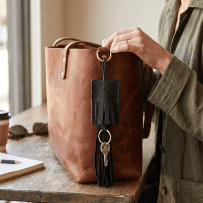 Leather key fob tassel by Will Leather Goods with black fringe and brass ring on a brown tote on Tampa Home & Garden Store