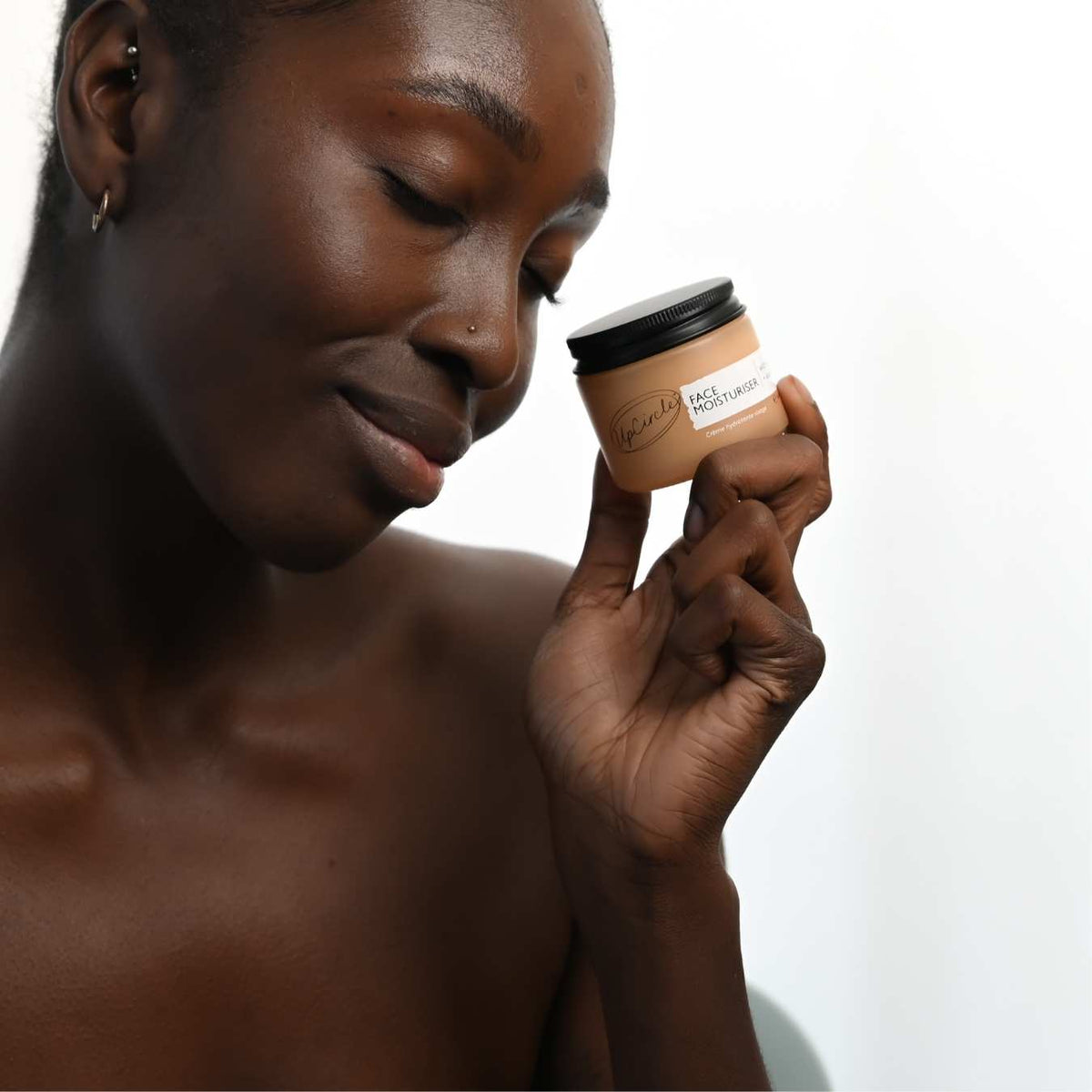 Face Moisturiser with Vitamin E by UpCircle, beige jar with black lid held near the face on Tampa Home & Garden Store