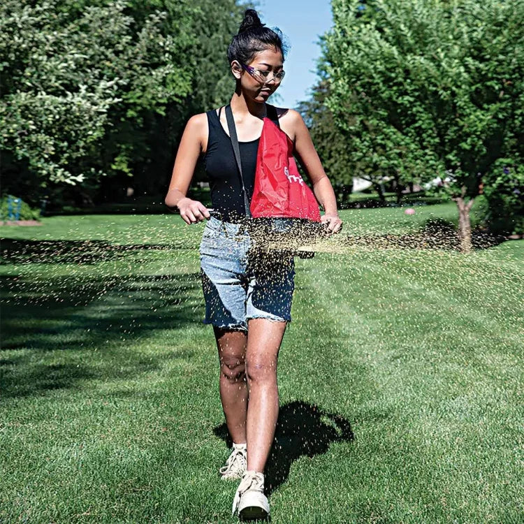 Earthway Over Shoulder Bag Spreader red nylon bag worn by a person in a sunny park on Tampa Home & Garden Store