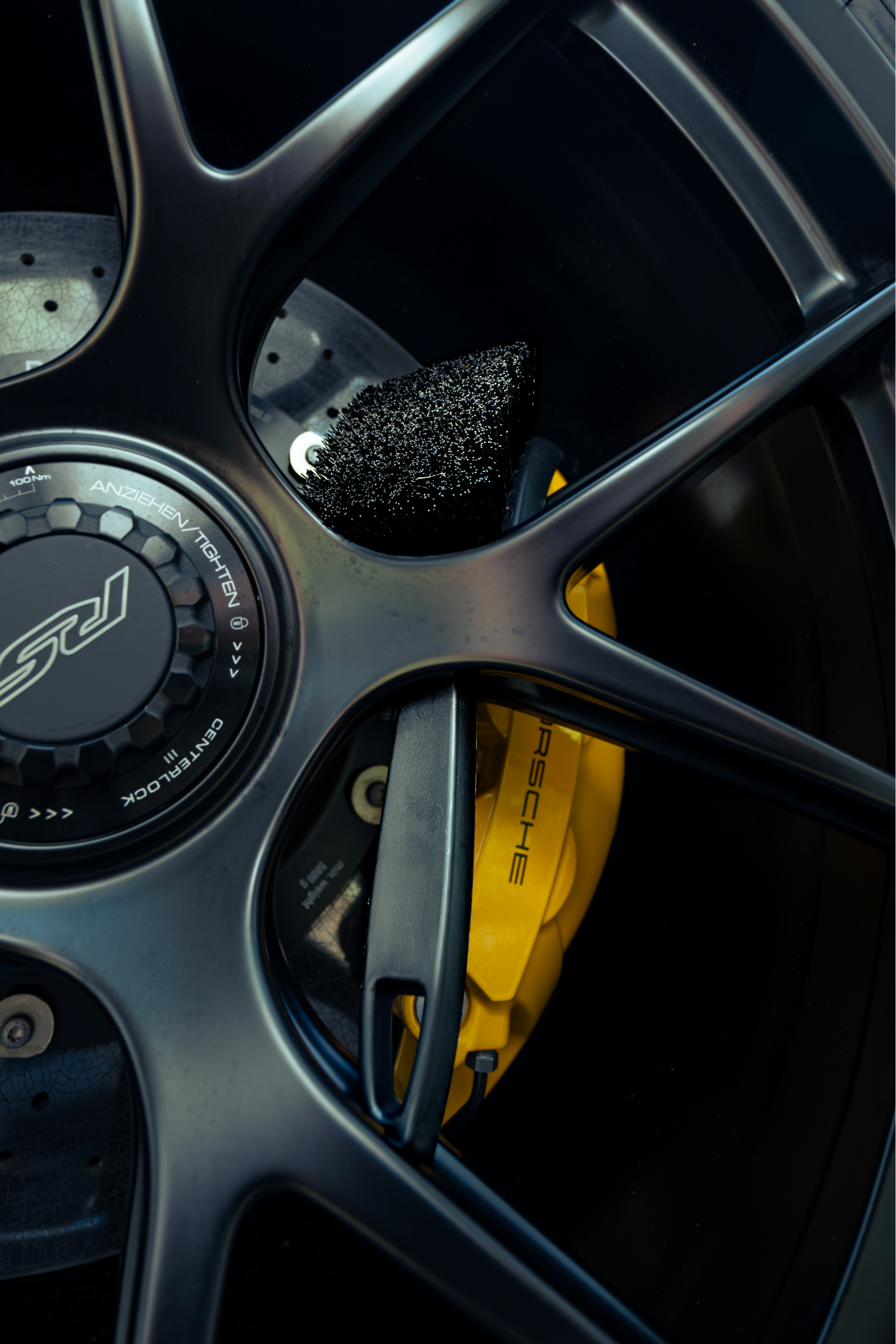 BLACKLINE® Stiff Bristle Tire Brush with black bristles beside a yellow Porsche brake caliper on a car wheel on Tampa Home & Garden Store