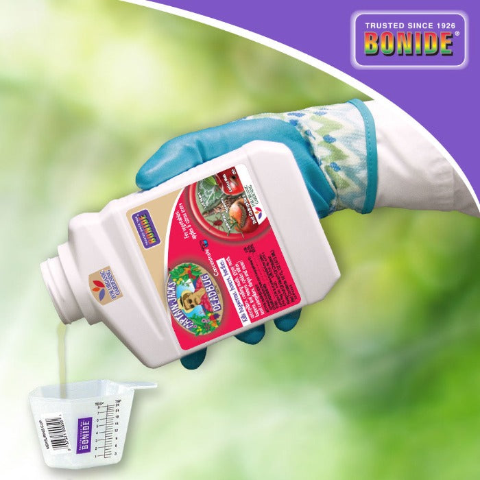Captain Jack's Dead Bug Brew concentrate in white Bonide bottle pours into a cup; gloved hand on Tampa Home & Garden Store