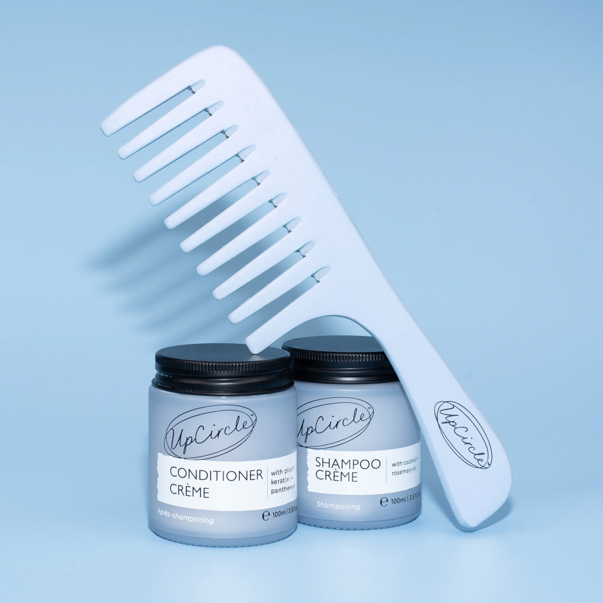 Haircare Duo + Bamboo Wide Tooth Comb UpCircle; white bottles and bamboo comb on blue background on Tampa Home & Garden Store