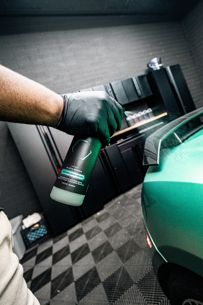 BLACKLINE® Waterless Wash bottle with teal label held by gloved hand beside a green car on Tampa Home & Garden Store