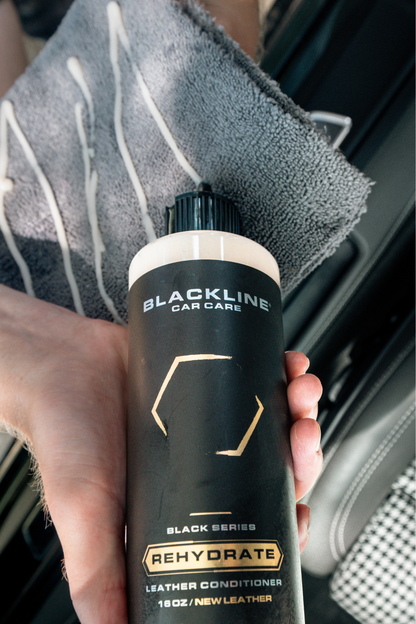 Leather conditioner bottle by Blackline Car Care, Rehydrate leather in vehicle, held beside a gray microfiber towel on Tampa Home & Garden Store