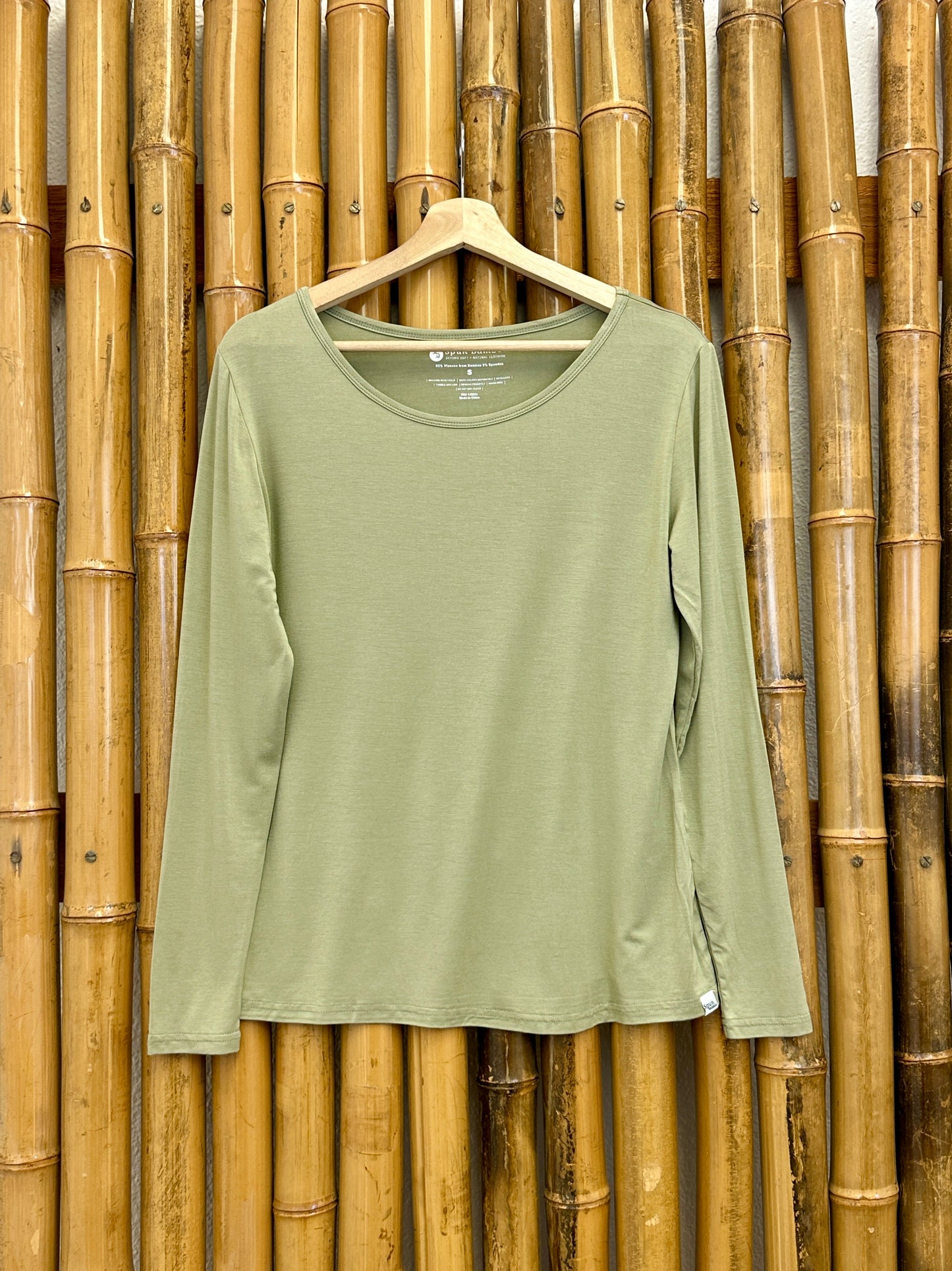 Women's Bamboo Long Sleeve T-Shirt Spun Bamboo in olive green fabric on a hanger amid bamboo on Tampa Home & Garden Store
