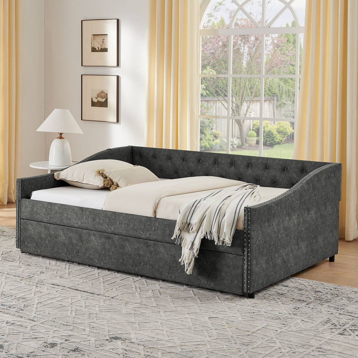 Upholstered grey daybed with nailhead trim and pull-out trundle in a bright bedroom on Tampa Home & Garden Store
