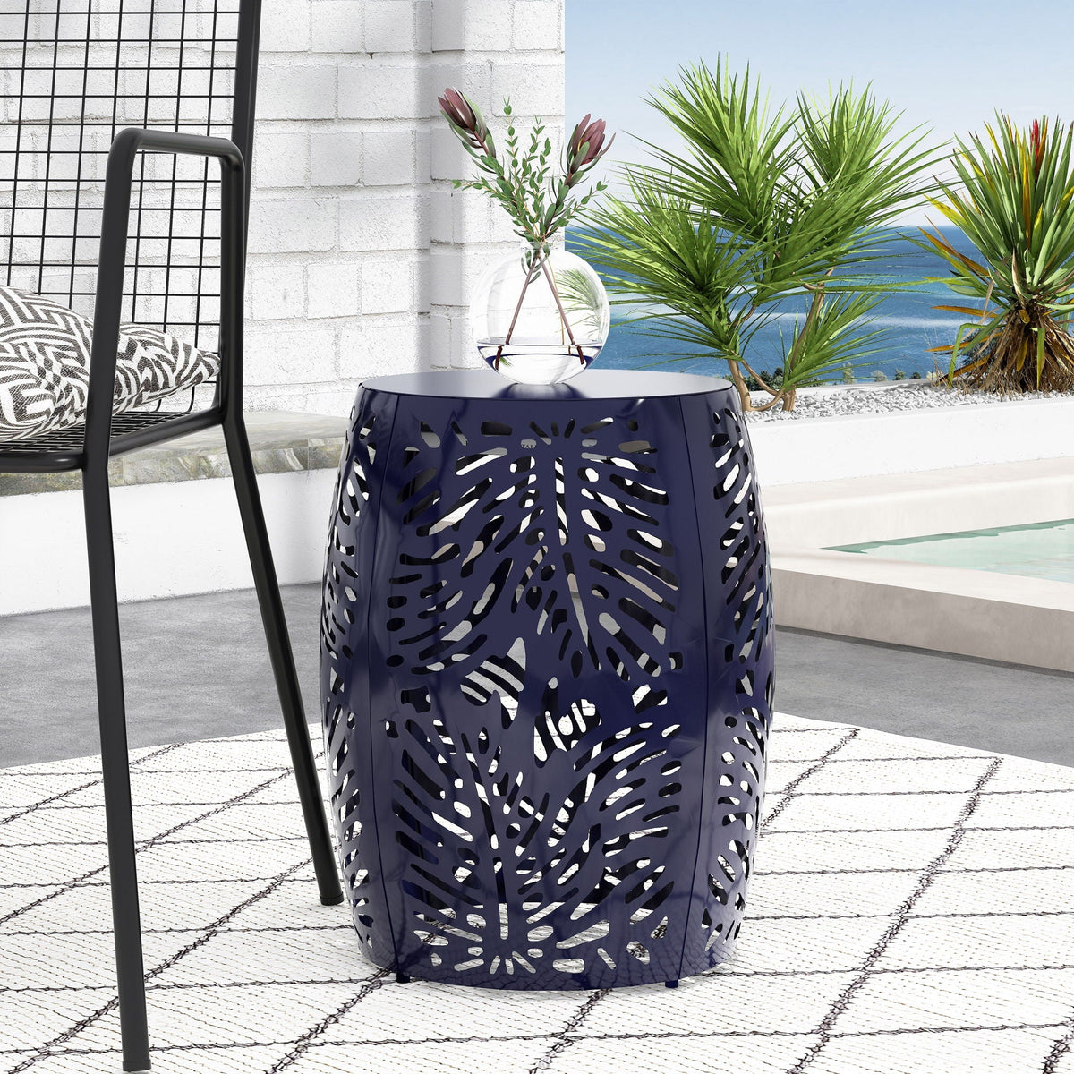 Blue palm-leaf cut-out metal outdoor end table with glass vase on a sunny patio scene on Tampa Home & Garden Store