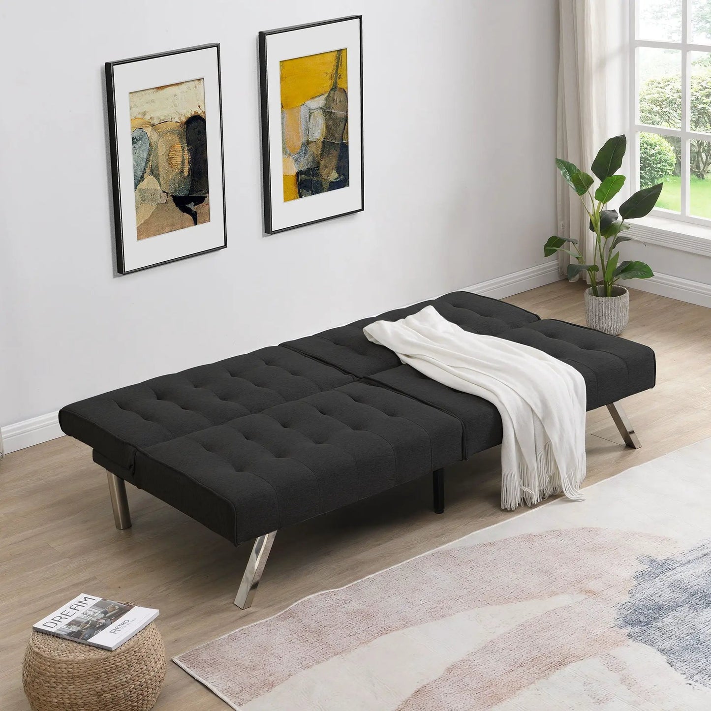 Futon sofa bed in charcoal black tufted fabric with metal legs in a bright modern room on Tampa Home & Garden Store