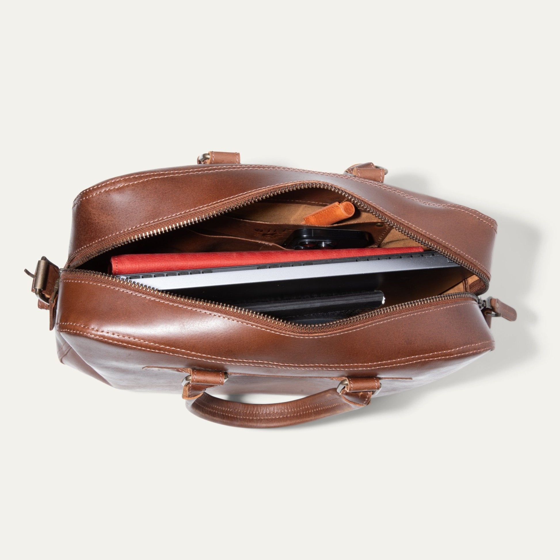 The Field Briefcase in brown leather with top zipper open showing laptop and red folder on Tampa Home & Garden Store