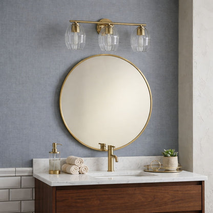 Luster 3-light vanity sconces with clear glass shades in satin gold above a round mirror on Tampa Home & Garden Store