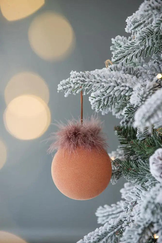 Orange glass Christmas ball ornament with fluffy pink fur topper hanging on snow-dusted pine on Tampa Home & Garden Store