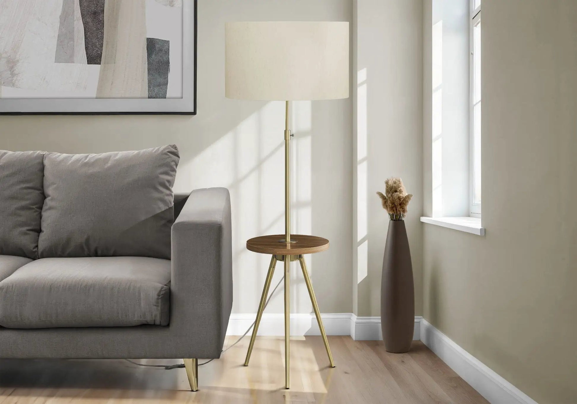 Floor lamp with brass tripod base and cream drum shade beside a gray sofa in living room on Tampa Home & Garden Store