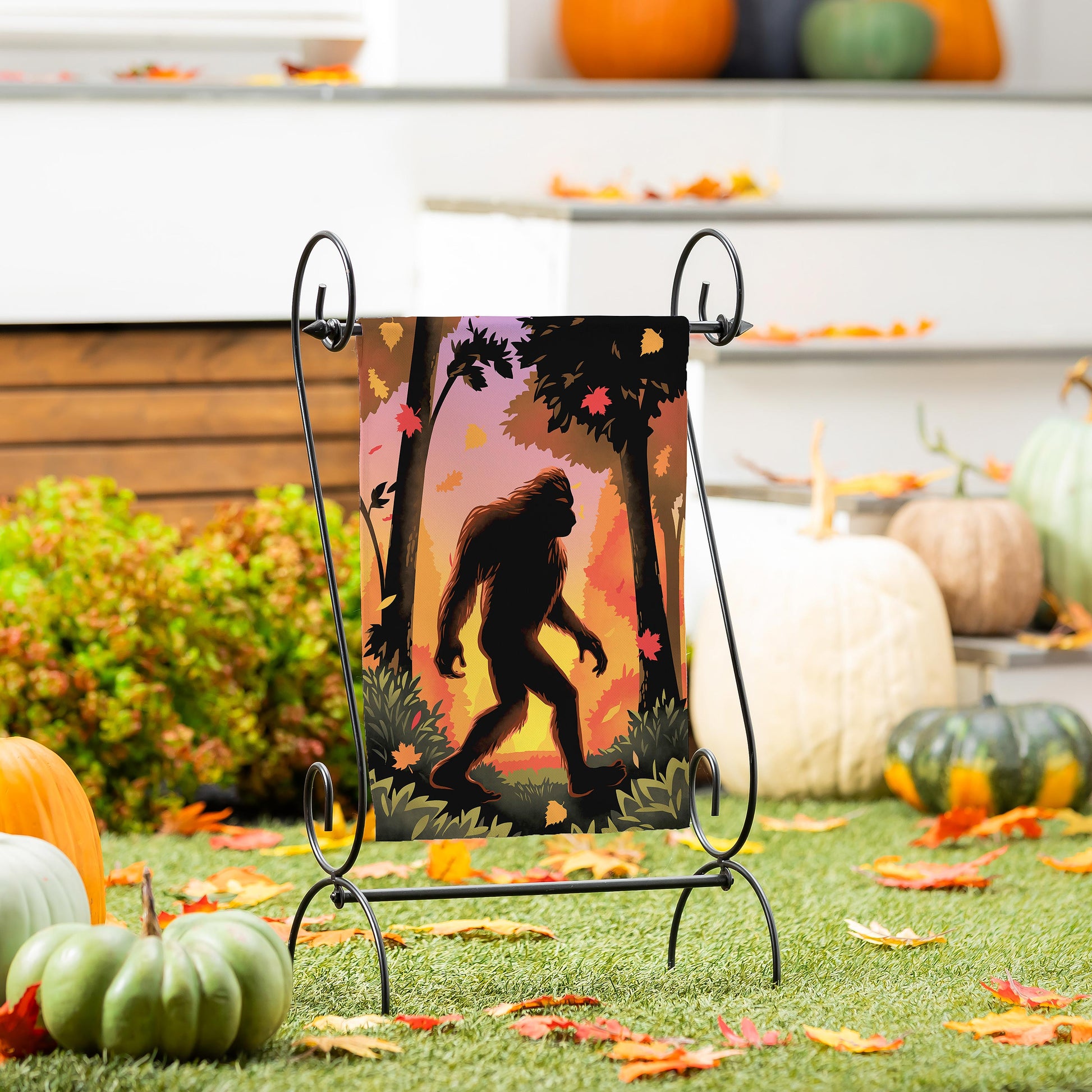 Bigfoot Fall Suede Garden Flag on a black metal stand with sunset silhouettes and autumn leaves on Tampa Home & Garden Store