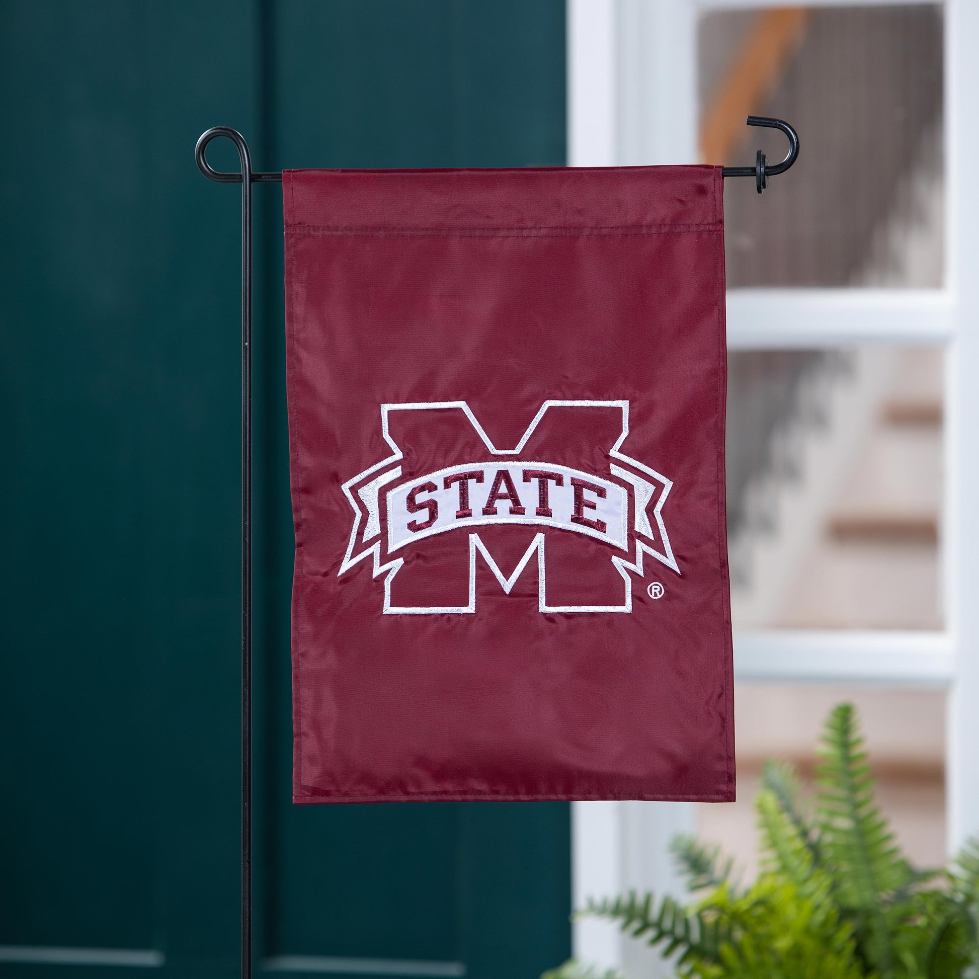 Mississippi State University applique flag in maroon with white emblem on a black metal stand on Tampa Home & Garden Store