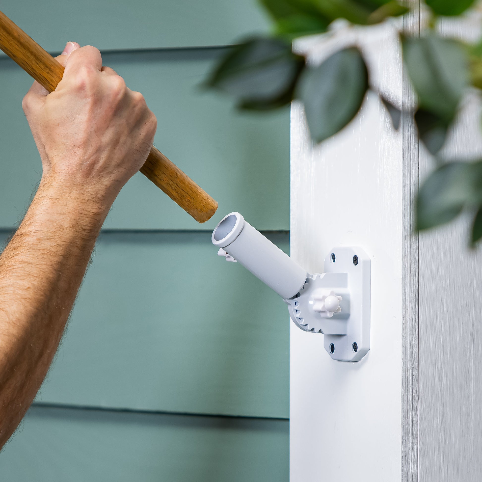 White metal flag bracket mounted on a white post as a hand grips a wooden flagpole on Tampa Home & Garden Store