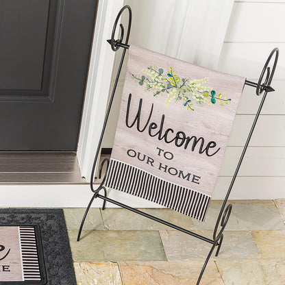Two wood-grain burlap welcome garden flags on a black metal stand with green leafy design on Tampa Home & Garden Store