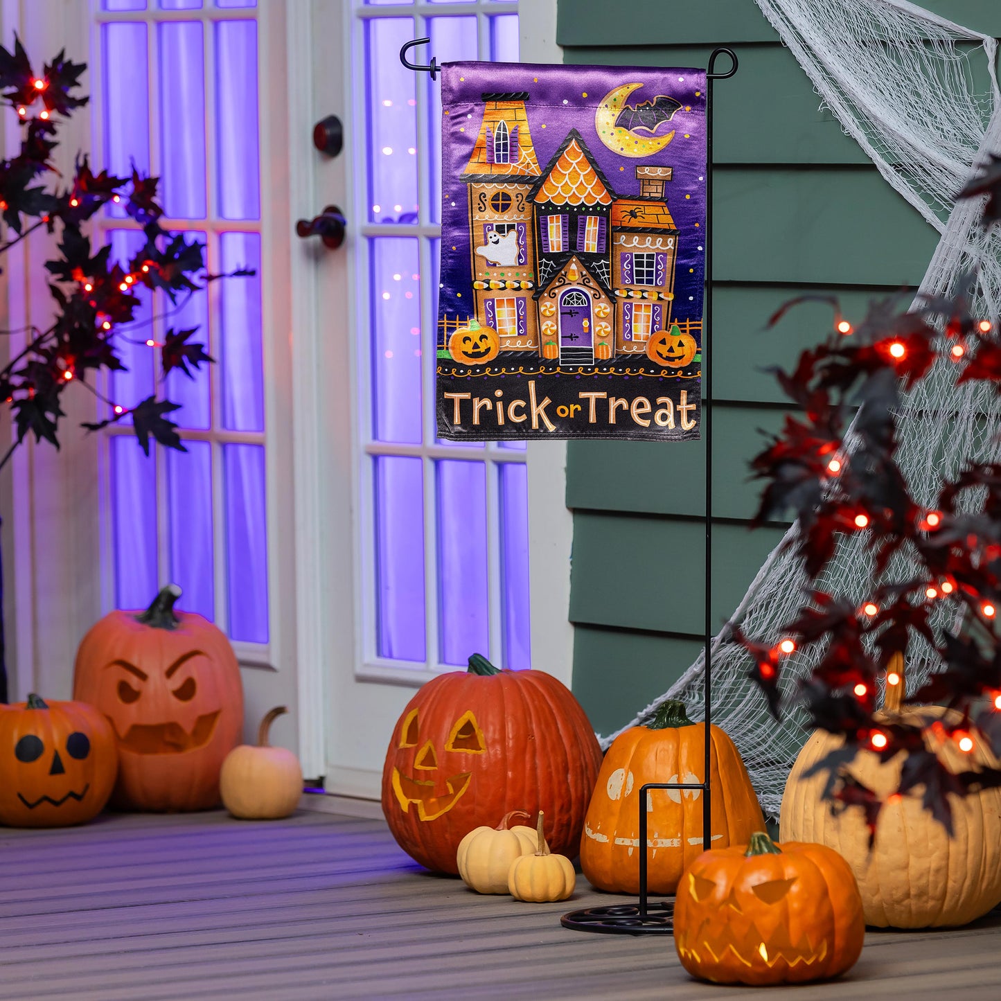 Trick or Sweets Lustre Garden Flag with purple night sky haunted house motif and pumpkins on porch on Tampa Home & Garden Store
