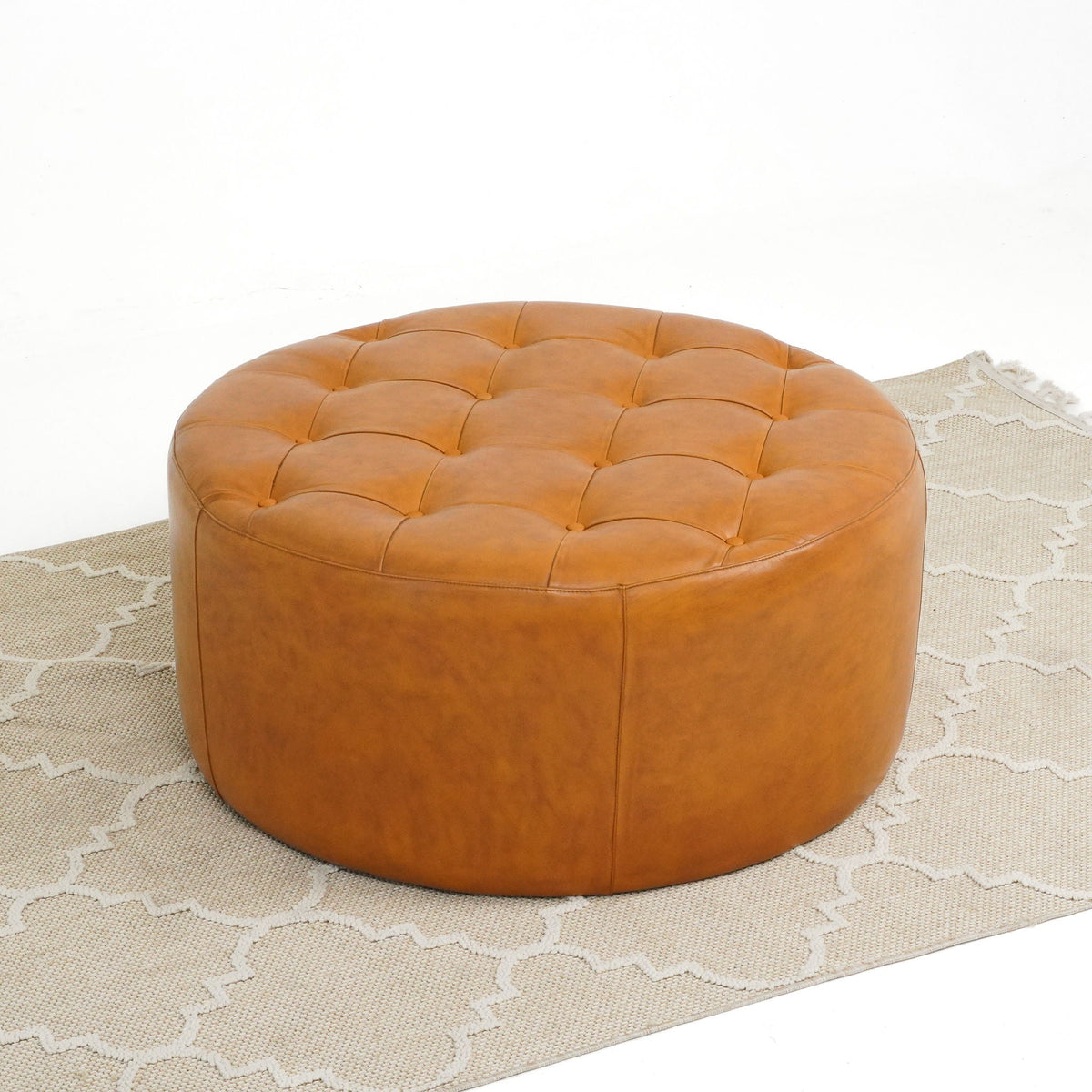 Light tan leather tufted round ottoman on beige rug with visible stitching on Tampa Home & Garden Store