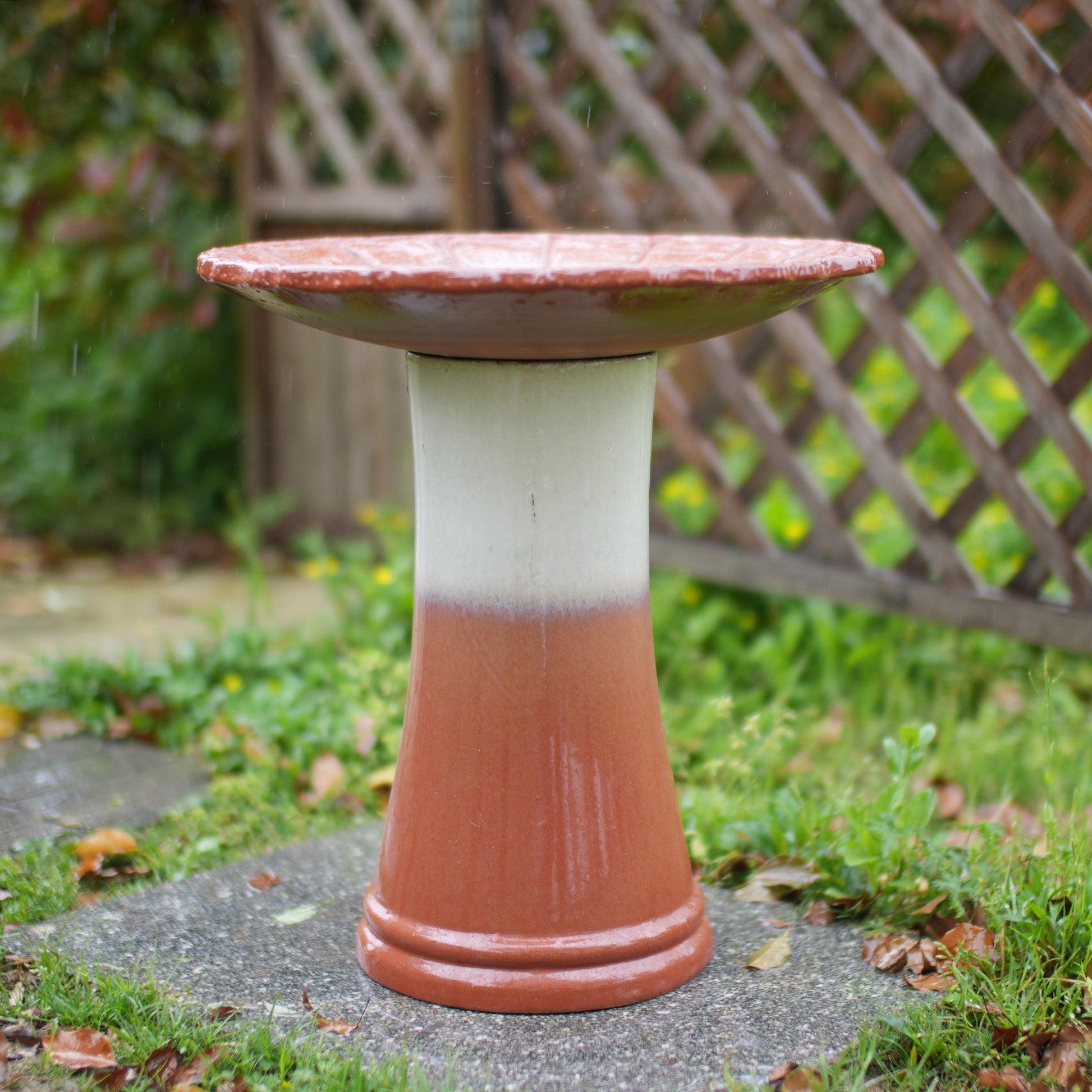 Handmade glazed ceramic bird bath on a terracotta pedestal with a red dish in a garden on Tampa Home & Garden Store
