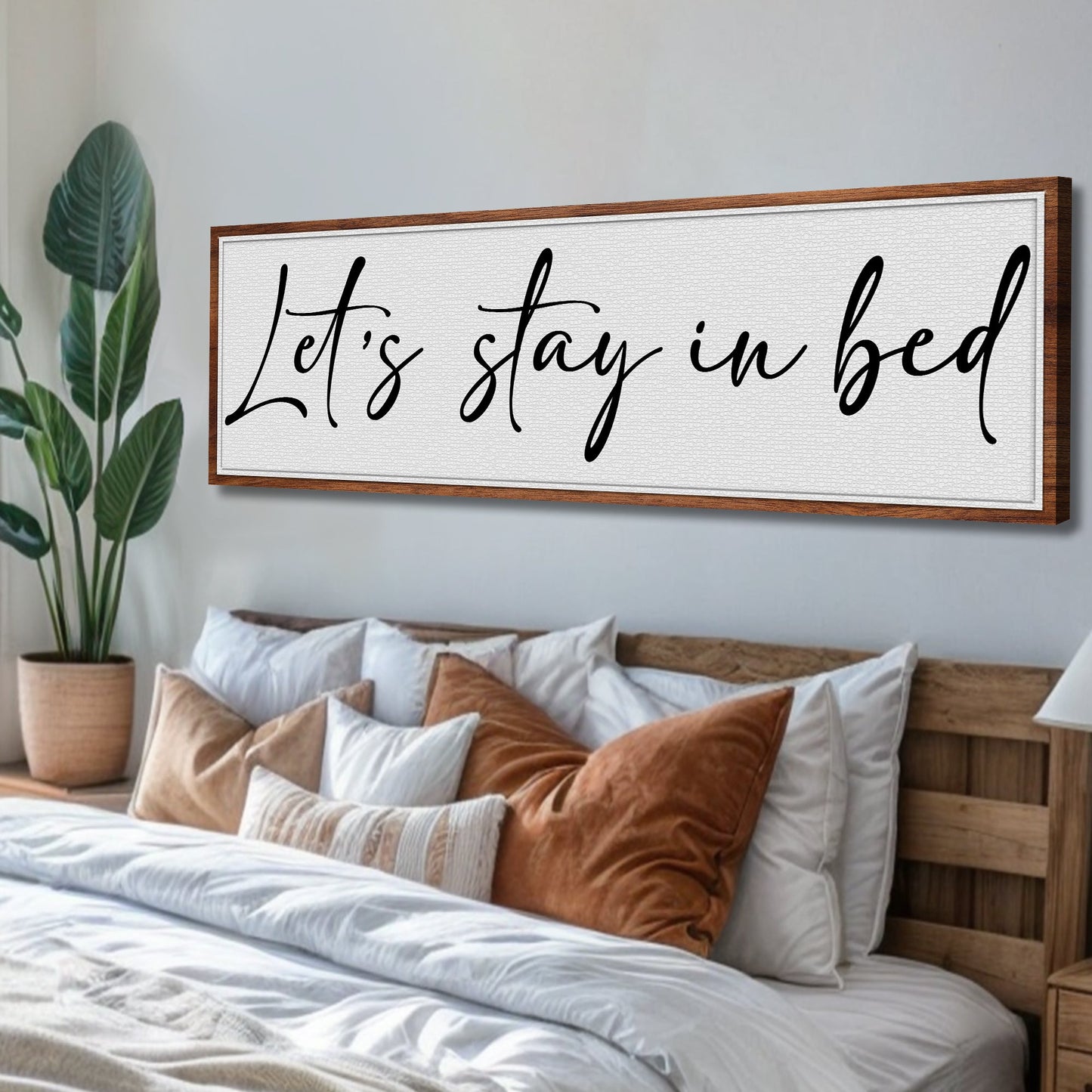 Let's Stay in Bed Bedroom Sign II canvas with black cursive text on white textured panel, wood frame in a bedroom on Tampa Home & Garden Store