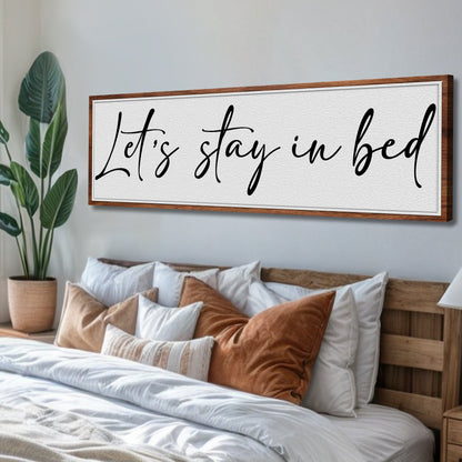 Let's Stay in Bed Bedroom Sign II canvas with black cursive text on white textured panel, wood frame in a bedroom on Tampa Home & Garden Store