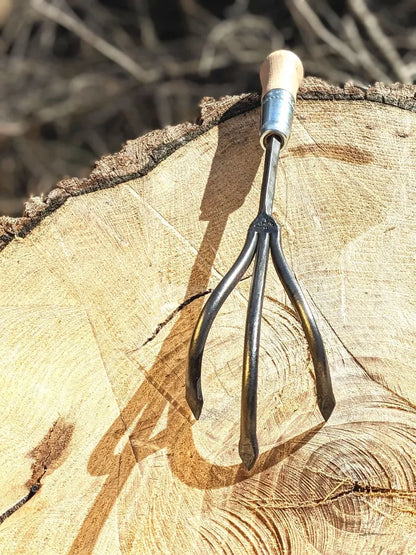 Homestead Iron 3-tine hand-forged cultivator with wooden handle and curved tines on a log stump on Tampa Home & Garden Store