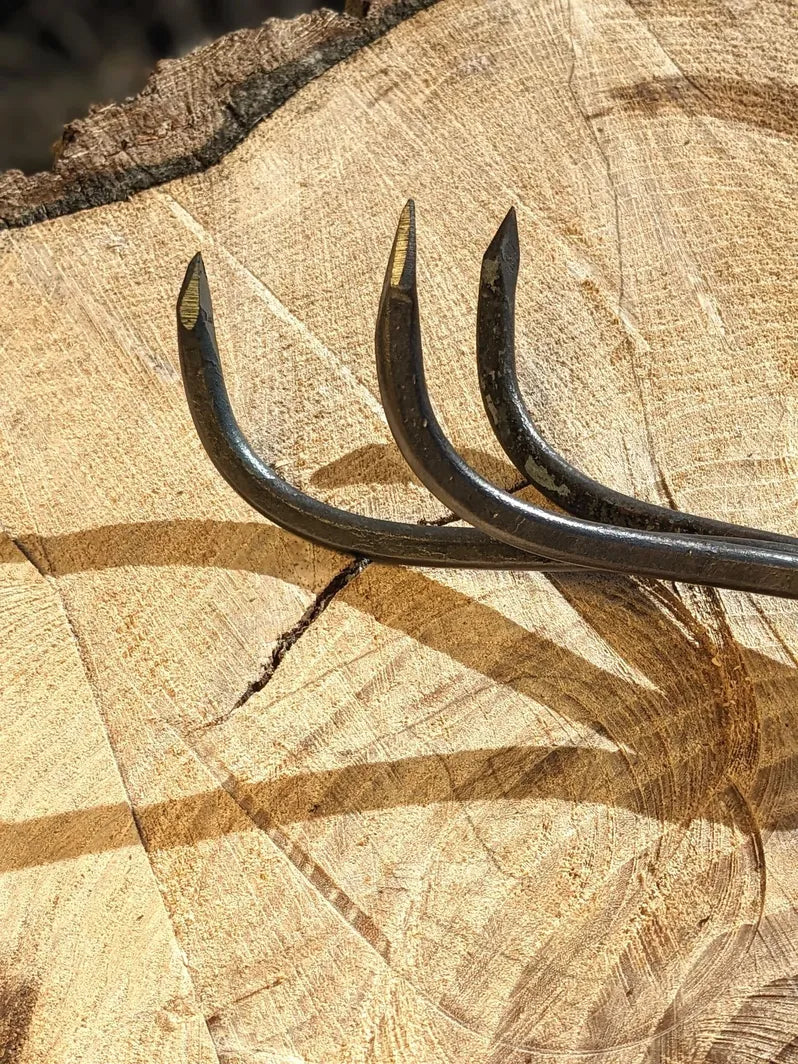 3 Tine hand forged cultivator garden tool with curved black steel tines on a cut log stump on Tampa Home & Garden Store