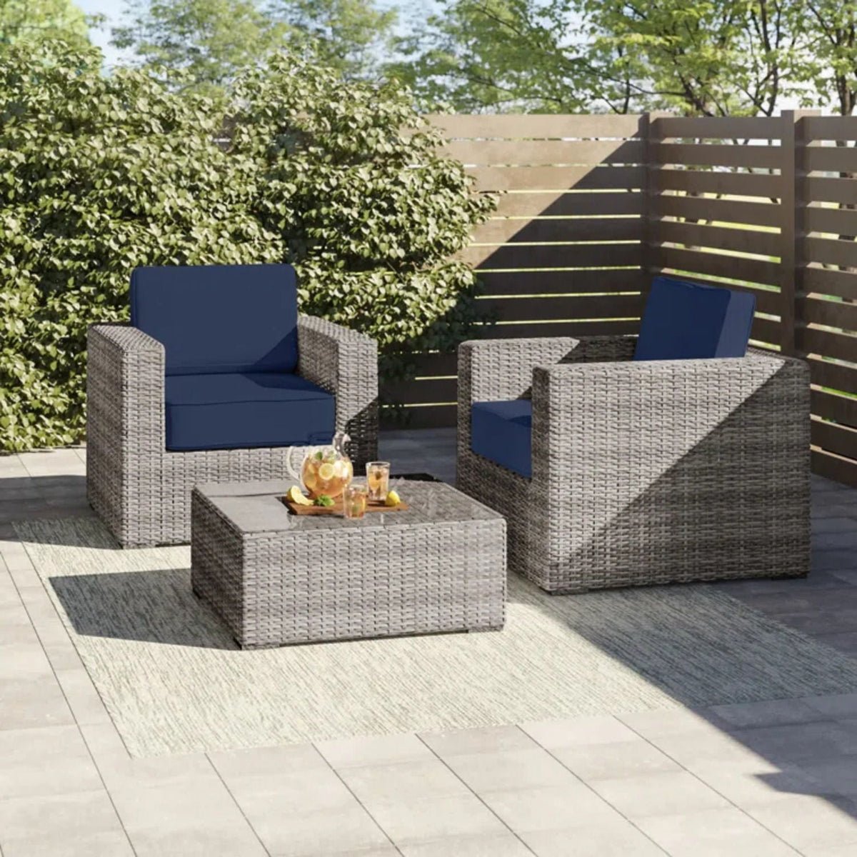 3 piece outdoor seating set with navy cushions on gray-brown wicker; two chairs and a coffee table on a patio with greenery on Tampa Home & Garden Store