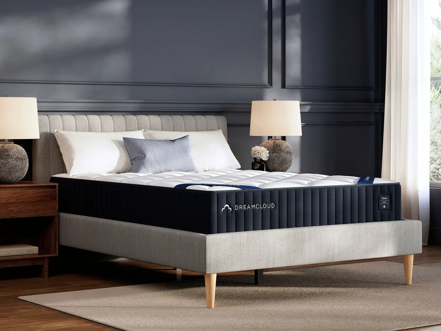 DreamCloud Classic Hybrid mattress on a gray upholstered platform bed with light wood legs in a dark paneled bedroom on Tampa Home & Garden Store