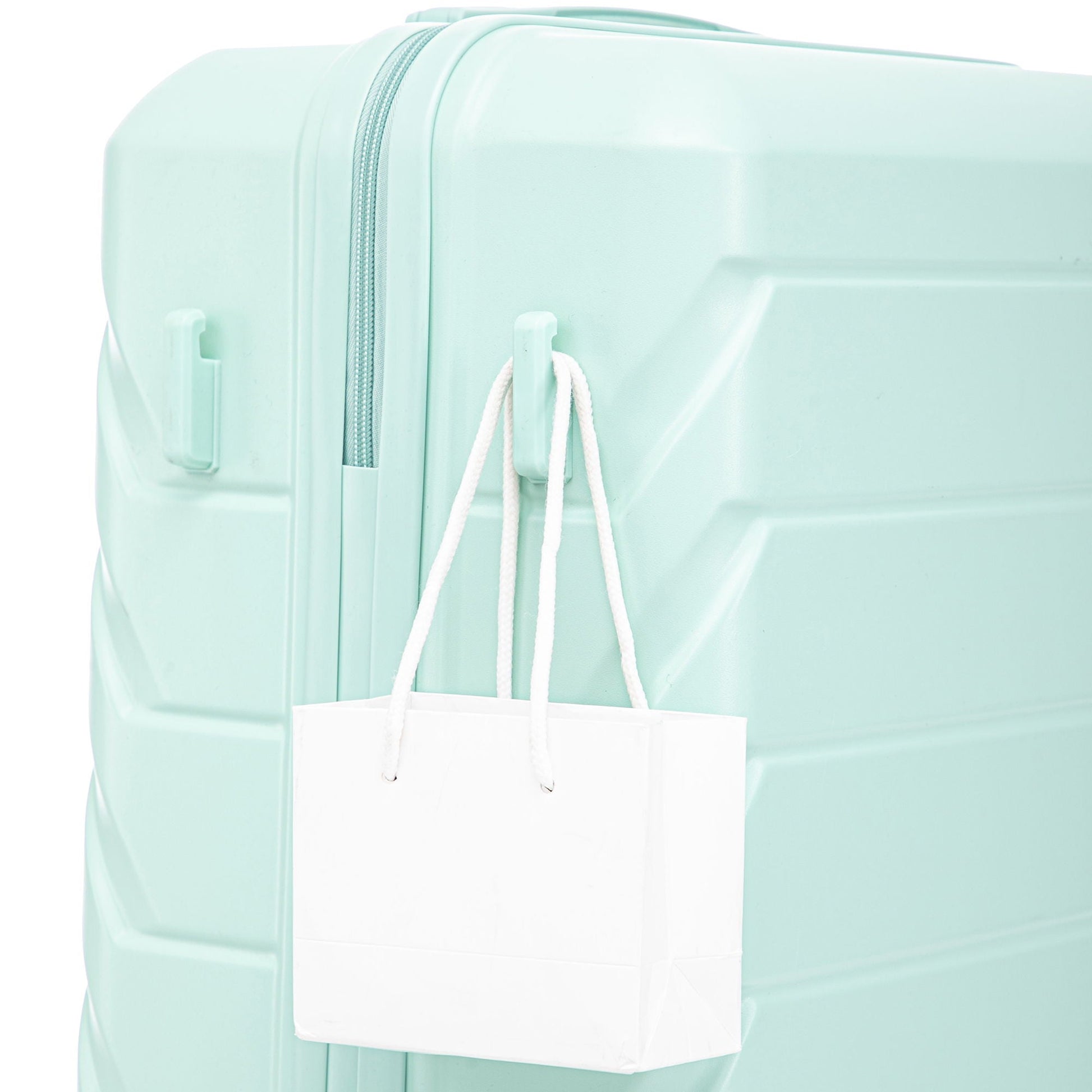 Mint green hard-shell luggage with a white shopping bag hanging from the handles on Tampa Home & Garden Store