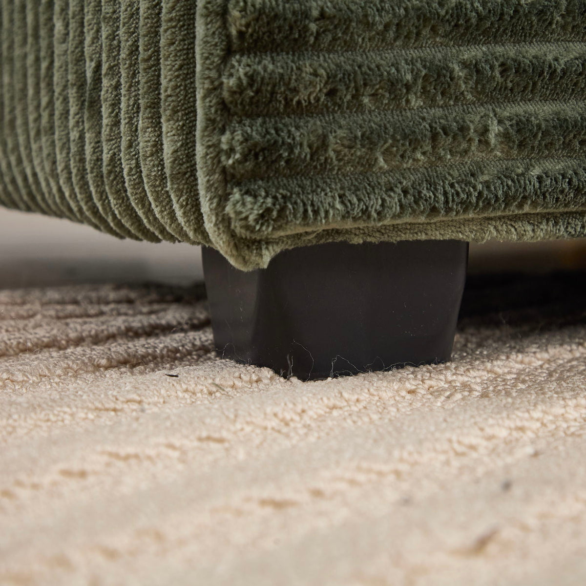 Green plush convertible sectional sofa bed base close-up showing black leg on beige carpet on Tampa Home & Garden Store