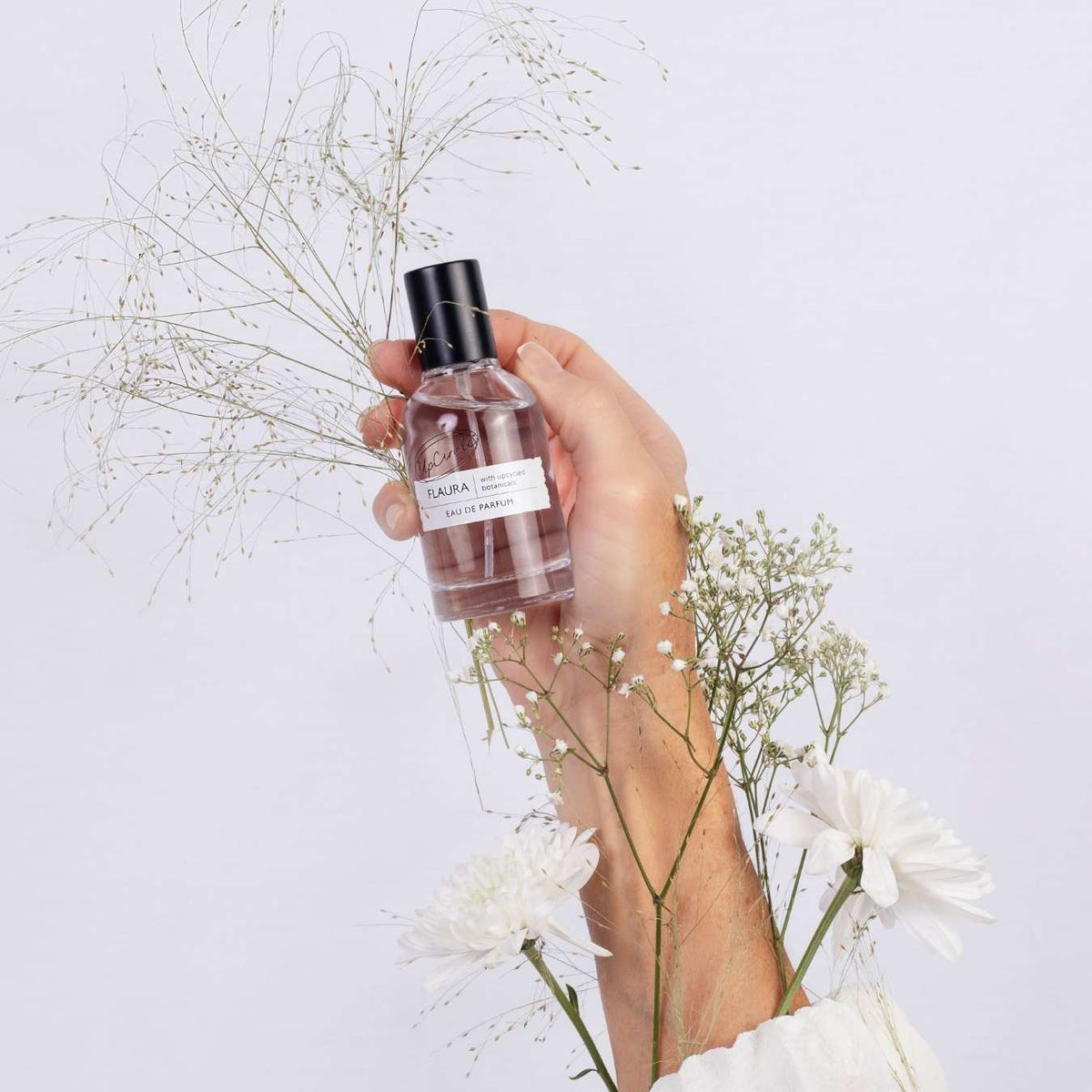 UpCircle Flaura Eau De Parfum bottle held in hand; pink liquid, black cap on Tampa Home & Garden Store