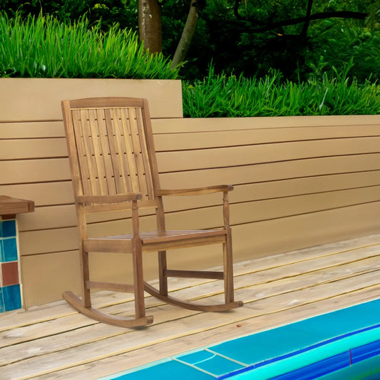 Arcadia outdoor teak wood rocking chair in natural finish on beige deck with greenery on Tampa Home & Garden Store