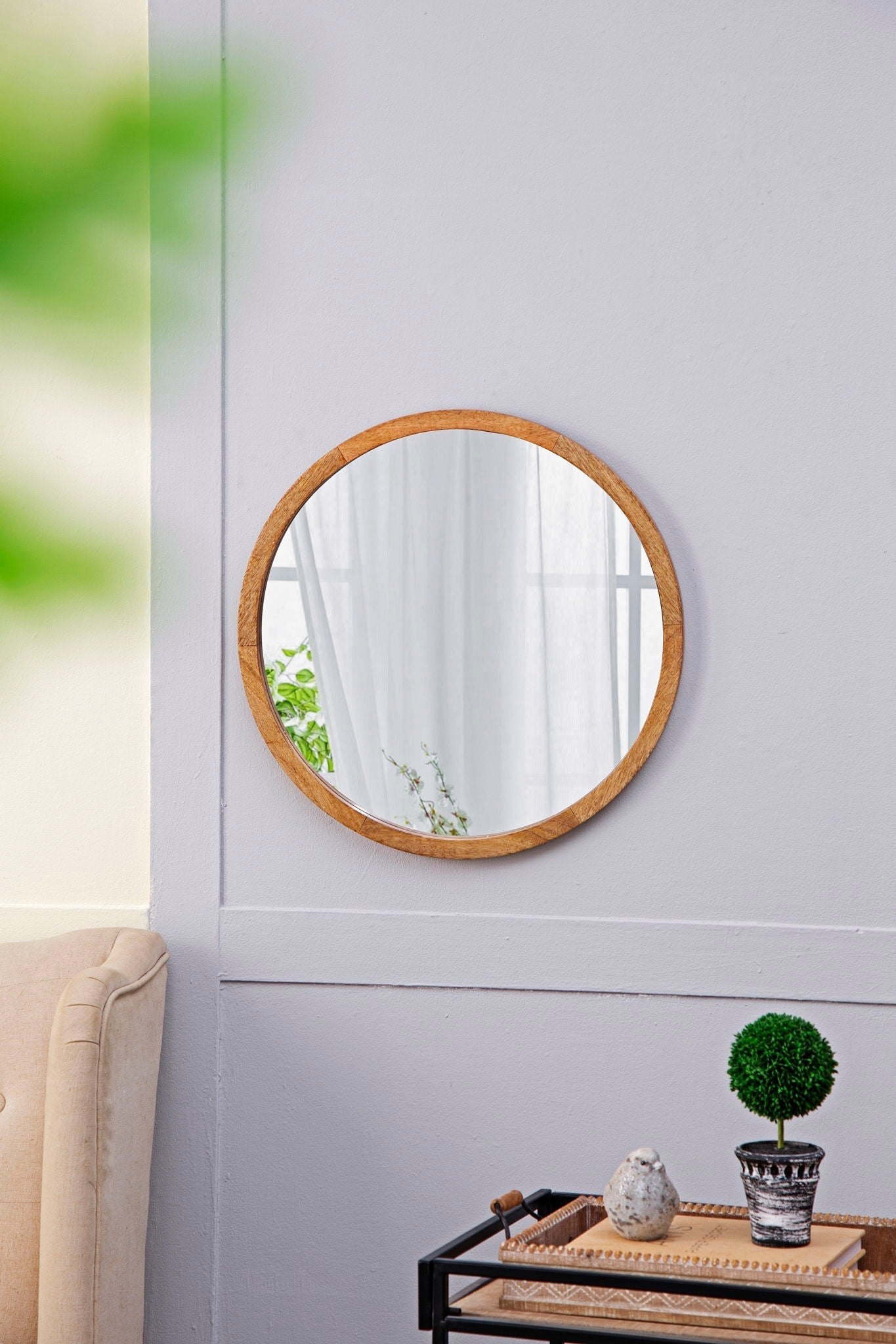 Round wall mirror with wooden frame on lavender wall reflecting curtains and plants on Tampa Home & Garden Store