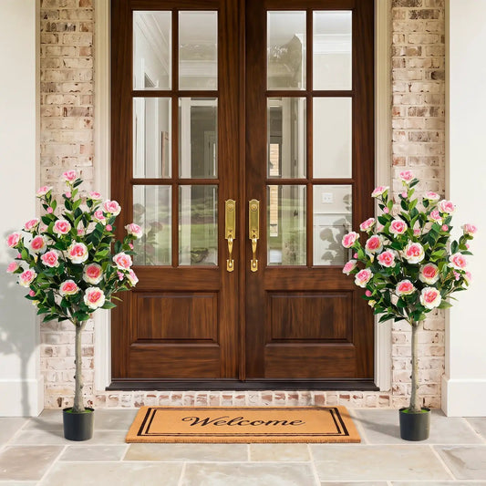 Two artificial camellia trees with 27 pink blossoms in cement pots flanking a wooden front door on Tampa Home & Garden Store
