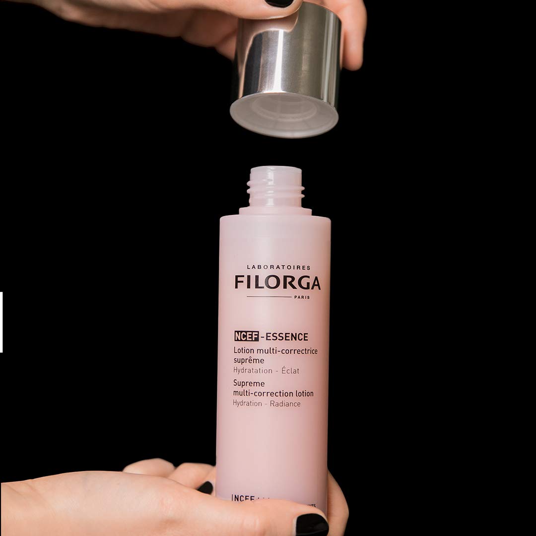 Filorga NCEF-ESSENCE pink face serum bottle with silver cap removed by hands on black backdrop on Tampa Home & Garden Store