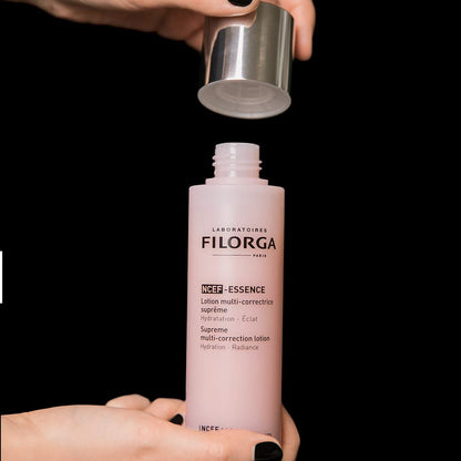 Filorga NCEF-ESSENCE pink face serum bottle with silver cap removed by hands on black backdrop on Tampa Home & Garden Store