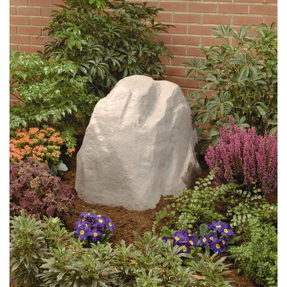 Sandstone Rock Valve Box Cover 53017 for underground irrigation amid shrubs and brick wall on Tampa Home & Garden Store