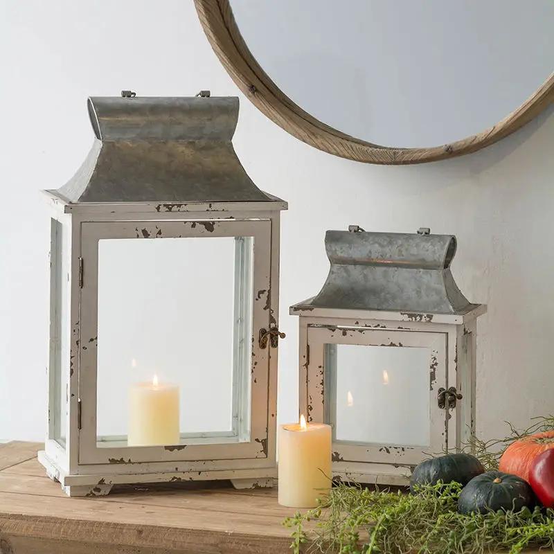 Two white distressed wooden lanterns with metal tops and glass panels, candles lit on a table on Tampa Home & Garden Store