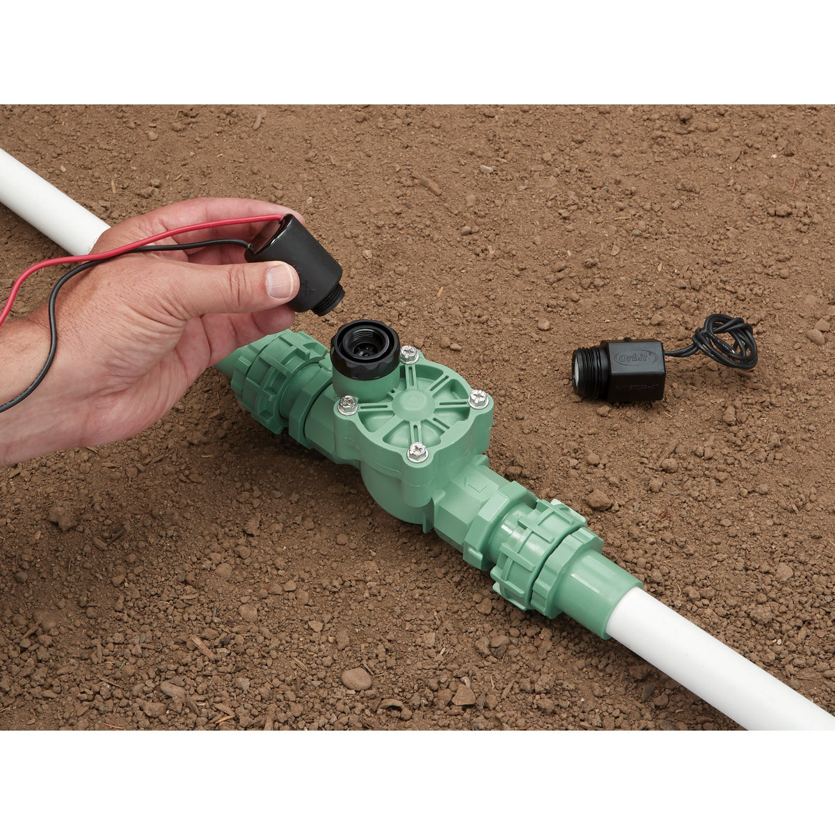 Battery-Powered Sprinkler Controller by Orbit Irrigation with red/black leads beside green irrigation valve on dirt on Tampa Home & Garden Store