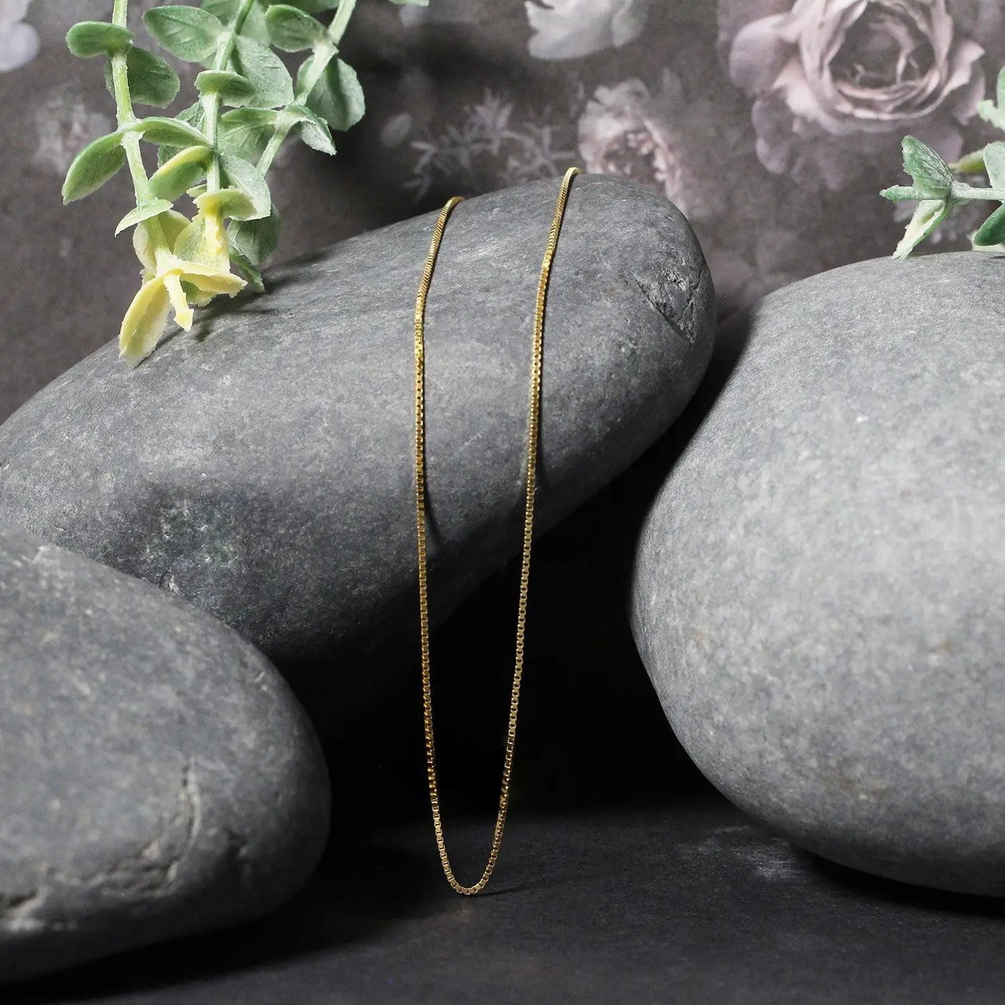 14k yellow gold classic box chain necklace 0.7mm by Bids.com resting on smooth gray stones on Tampa Home & Garden Store