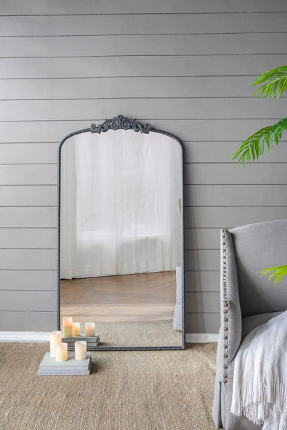 Arch mirror with ornate dark Baroque frame leaning against gray wall beside a beige chair on Tampa Home & Garden Store