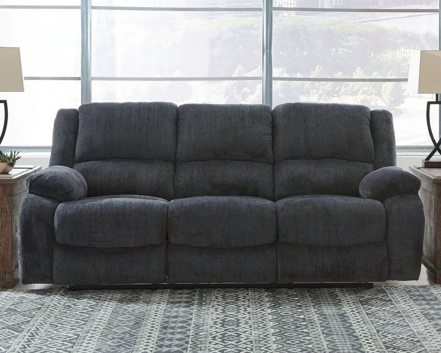 Draycoll reclining sofa in dark charcoal gray fabric with plush cushions in front of large windows on Tampa Home & Garden Store