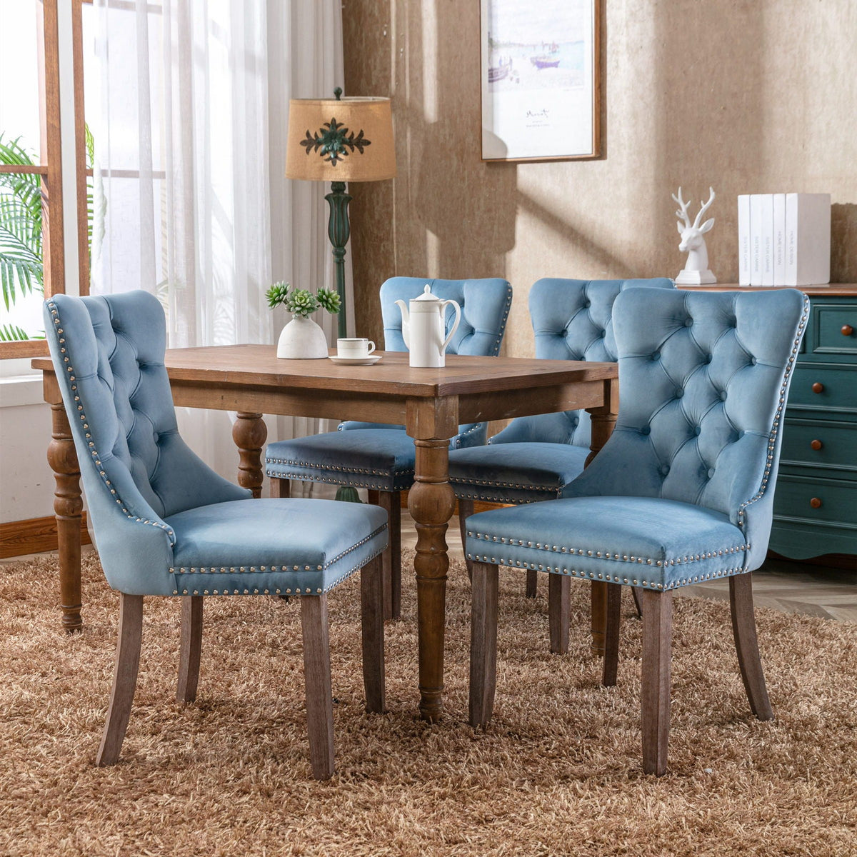 Set of four blue velvet tufted dining chairs with nailhead trim around a wooden table on Tampa Home & Garden Store