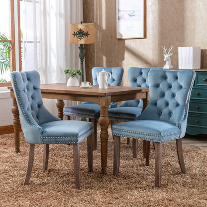 Set of four blue velvet tufted dining chairs with nailhead trim around a wooden table on Tampa Home & Garden Store