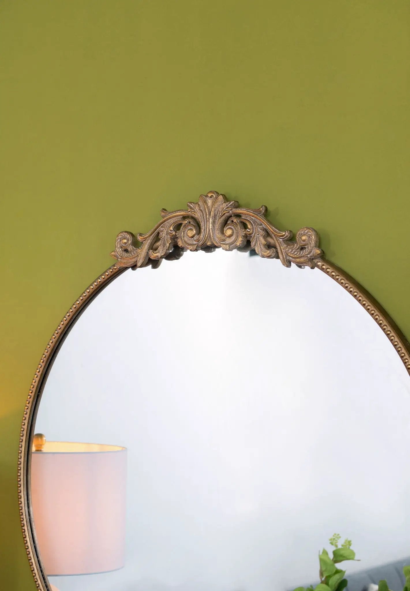 Classic design wall mirror with Baroque-inspired ornate gold frame leaning against a green wall on Tampa Home & Garden Store