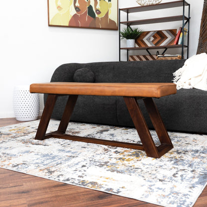 Light brown upholstered bench with hand stitching and dark wood legs in living room on Tampa Home & Garden Store