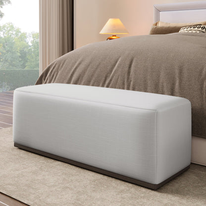 Footstool bench in light gray fabric with dark wood base at bed foot in a neutral bedroom on Tampa Home & Garden Store