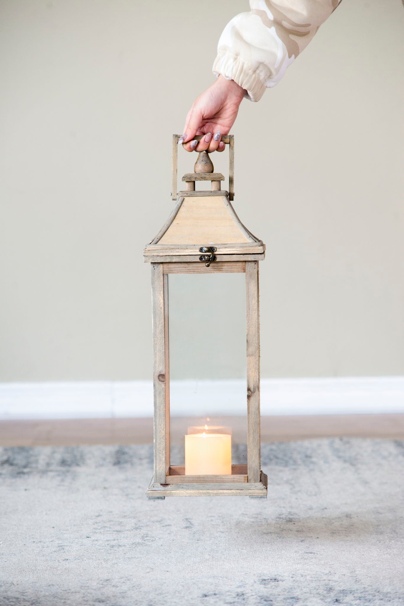 Ivory candle lantern with weathered wooden frame and glass panes, lit candle inside, held by hand on Tampa Home & Garden Store