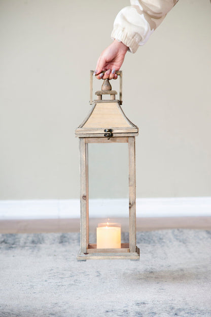 Ivory candle lantern with weathered wooden frame and glass panes, lit candle inside, held by hand on Tampa Home & Garden Store